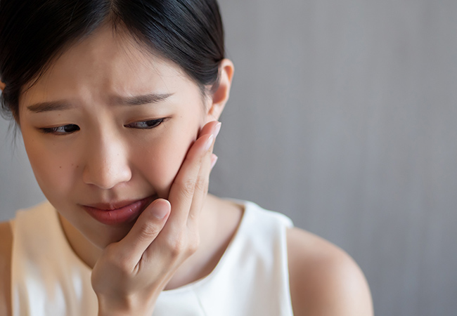 口腔内に痛みを感じ頬に手を当てる女性